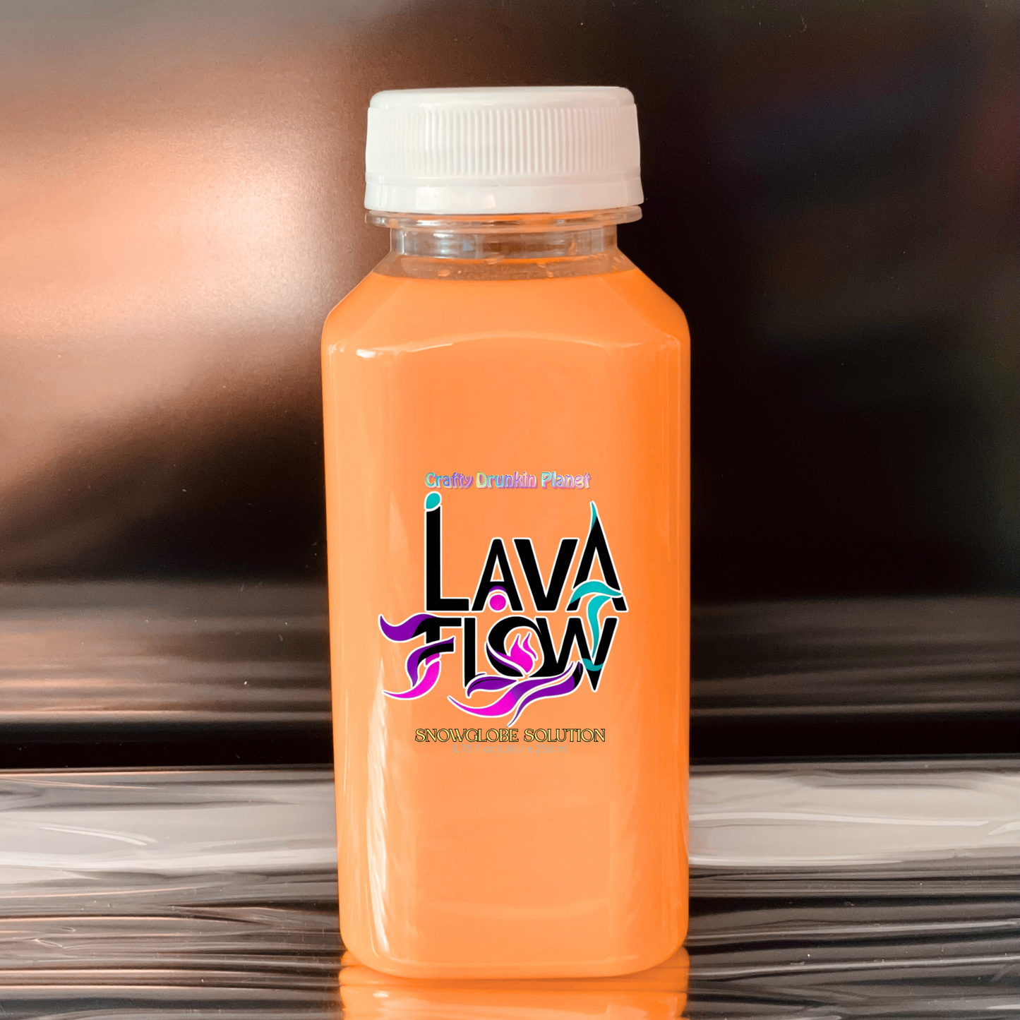 Orange bottle of Lava Flow snowglobe solution product on a reflective surface with a blurred background
