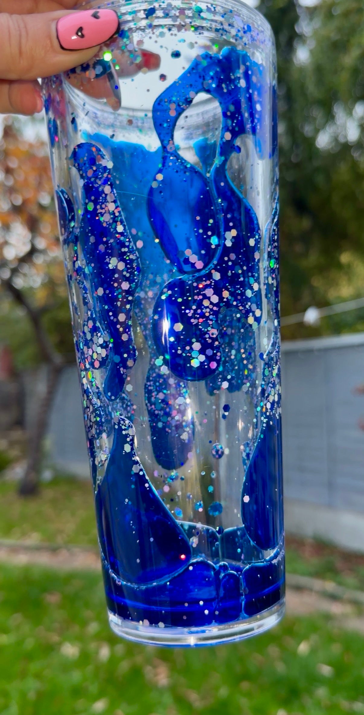 acrylic snowglobe tumbler with blue lava drip flow solution held by a hand outdoors
