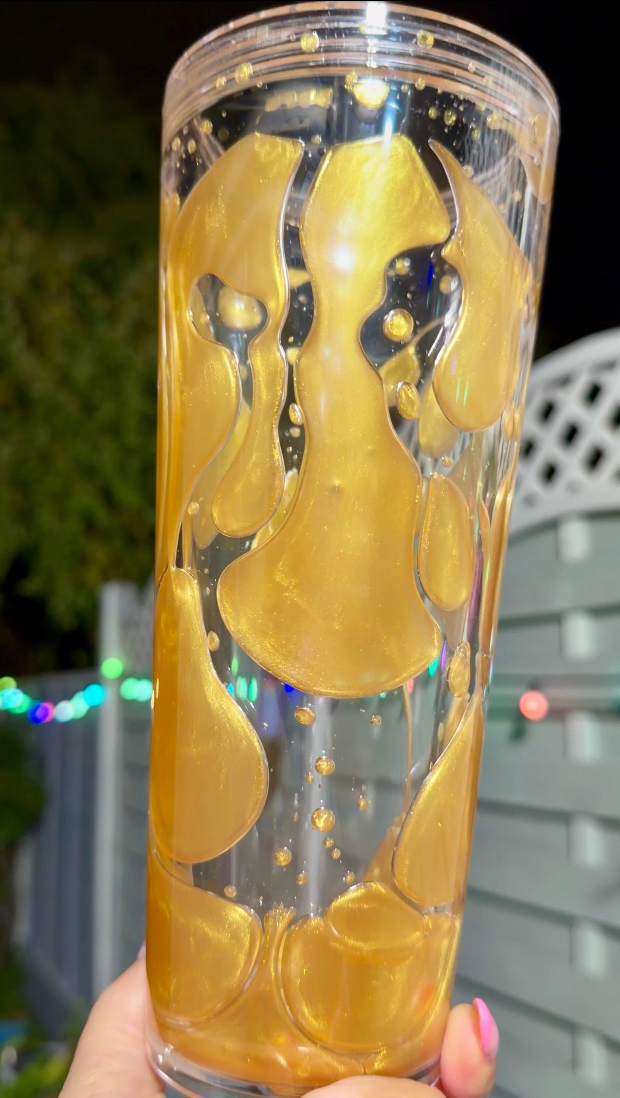 Clear tumbler with gold lava drip flow solution held by a hand 