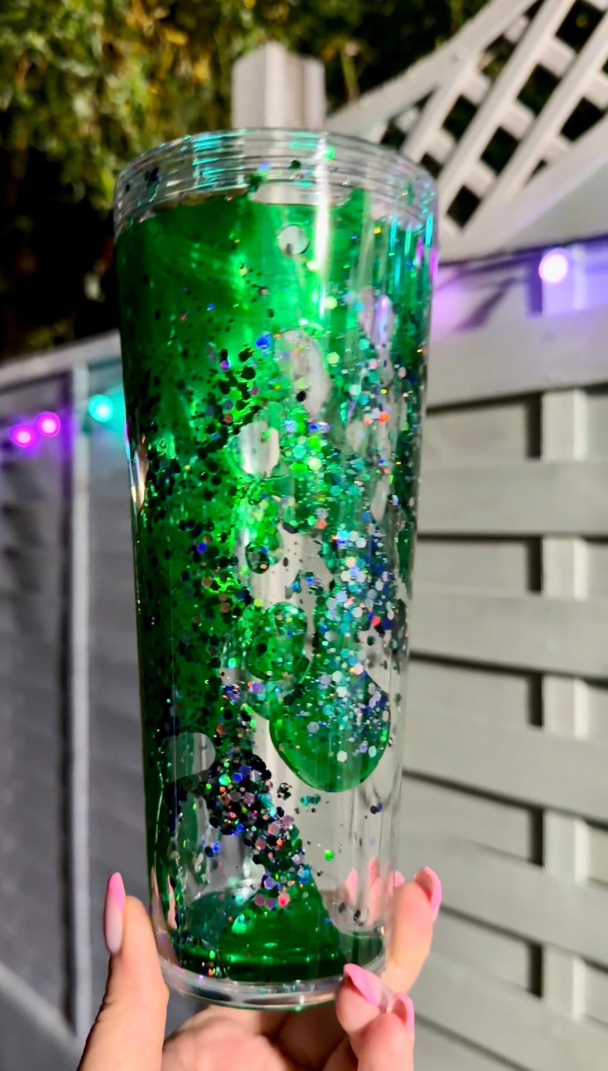 Green glittery tumbler with green lava drip flow solution held by a hand 