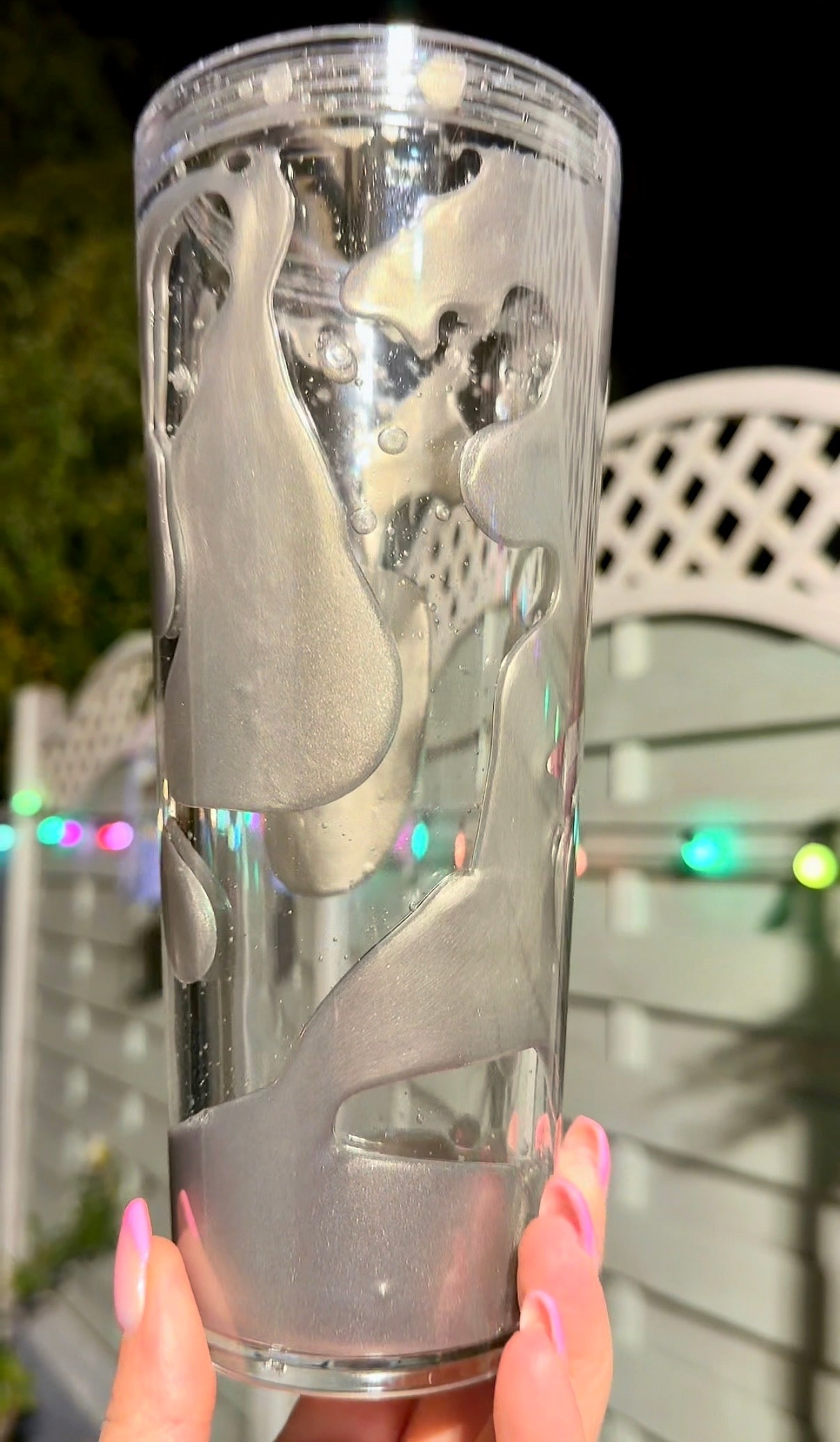 Clear tumbler with silver gold lava drip flow solution held by a hand outdoors